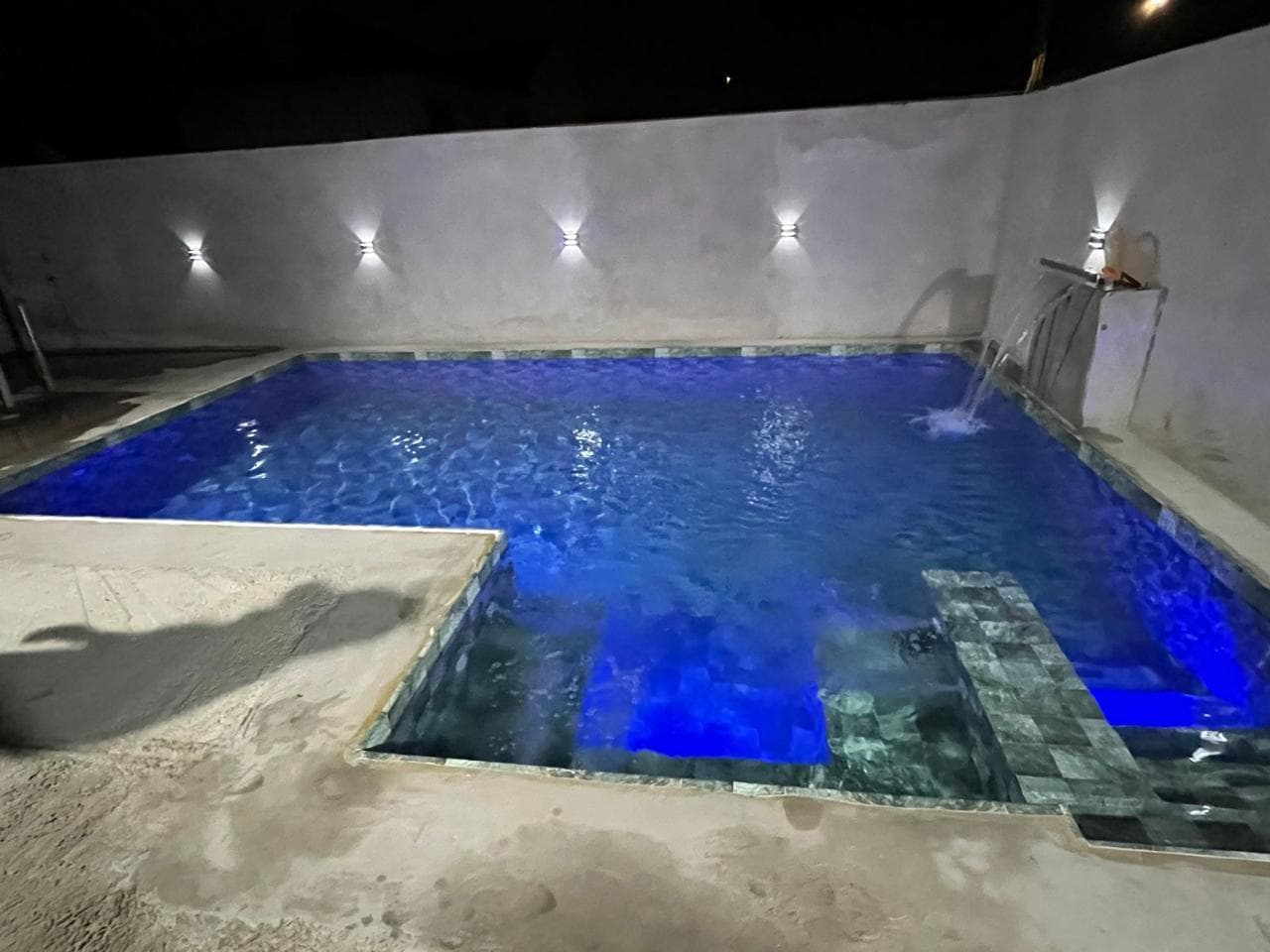 Piscina residencial iluminada em azul com cascata