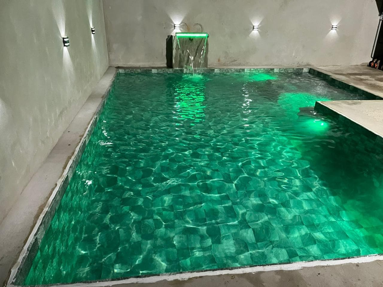 Piscina residencial com iluminação verde e cascata